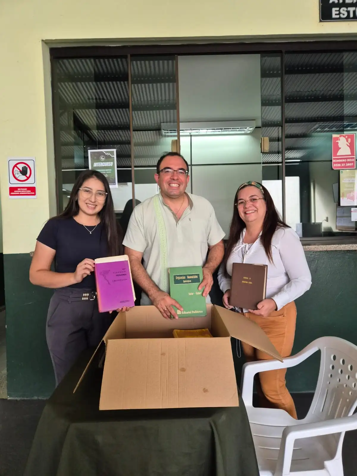 Estudiantes de medicina recibiendo textos académicos y atlas de anatomía en una biblioteca universitaria.
